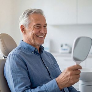 Senior dental patient looking at his smile in mirror