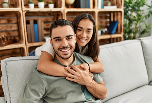 Man on couch being hugged from behind by woman