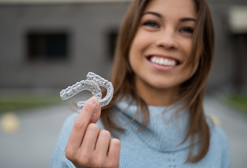 Smiling woman holding two clear aligners