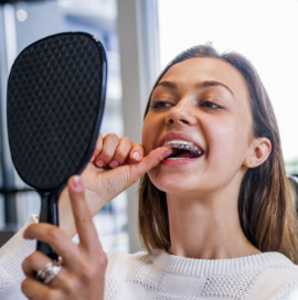 Woman using handheld mirror to put in clear aligners