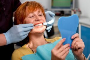 Woman with implant smiling in dentist's chair. 